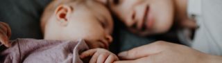 Happy young mother touching her newborn baby girl, lying on sofa indoors at home.